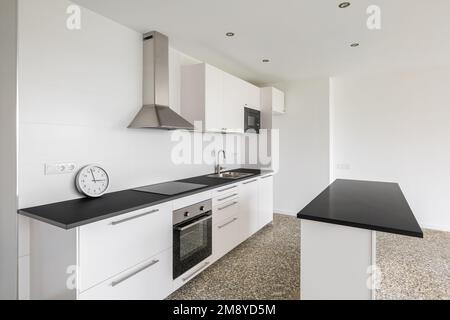 Große geräumige Küche mit Holzmöbeln in Schwarz und Weiß. Arbeitsflächen aus schwarzem Marmor. Küchenelektronik und Spülbecken aus gebürstetem Metall. Geräumig Stockfoto