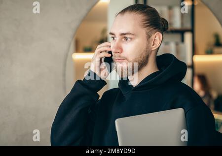 Ein junger Geschäftsmann mit Bart spricht über ein Smartphone. Stockfoto