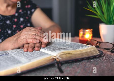 Eine alte Frau liest die Bibel, die Hände sind dicht. Stockfoto