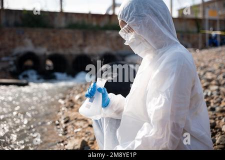 Ökologe entnehmen wassertoxische Chemikalien aus dem Fluss mit Reagenzglas und weisen weißen Rauch auf Stockfoto