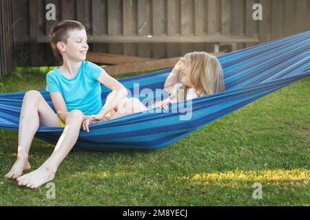 Kinder, Bruder und Schwester, spielen im Garten auf einer Hängematte. Stockfoto