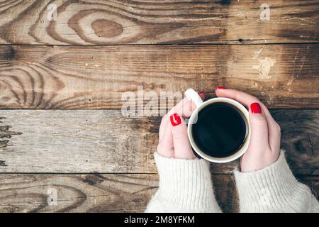 Weibliche Hände halten eine Tasse Kaffee auf einem hölzernen Hintergrund, flach liegend. Stockfoto
