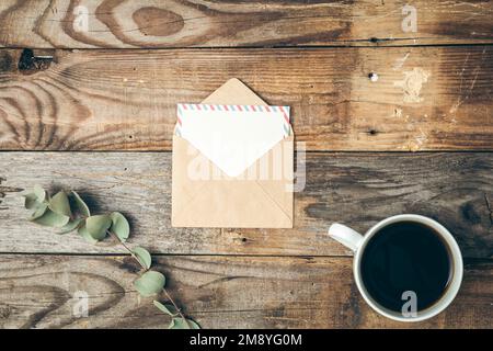 Umschlag, eine Tasse Kaffee und ein Zweig Eukalyptus auf einem hölzernen Hintergrund. Stockfoto