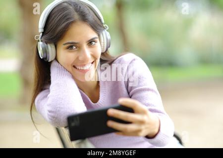 Glückliche Frau, die Musik hört und dich im Park ansieht Stockfoto
