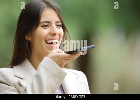 Glückliche Frau, die im Winter Spracherkennung mit Smartphone verwendet Stockfoto