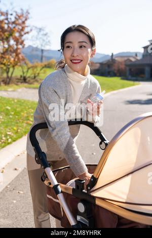 Junge Mutter schiebt einen Kinderwagen für einen Spaziergang Stockfoto