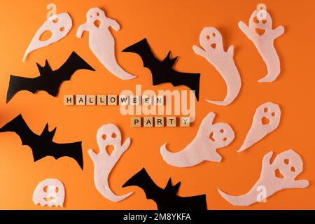 Weiße Geister und Fledermäuse für Halloween-Party. Einwickelpapier auf orangefarbenem Hintergrund, Draufsicht. Ein unheimlicher Cartoon-Whisper. Handgefertigt. Stellt die Figuren ein. Wort aus Holz. Stockfoto