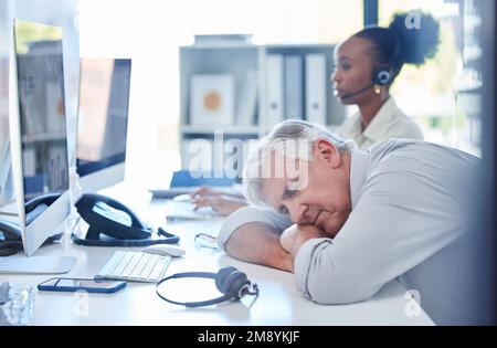 Es war ein langsamer Tag, ich könnte genauso gut schlafen. Ein erfahrener Callcenter-Agent schläft an seinem Schreibtisch in einem Büro. Stockfoto