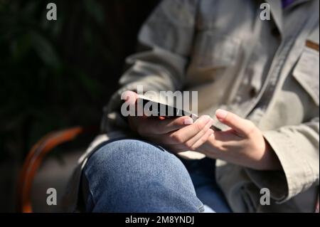 Eine weibliche Hand hält ein Smartphone und verwendet ihr modernes Mobiltelefon, während sie sich im Café entspannen. Zugeschnittenes Bild Stockfoto