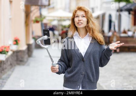 Junge rothaarige, schöne Frau, die läuft und ihr Handy benutzt Stockfoto