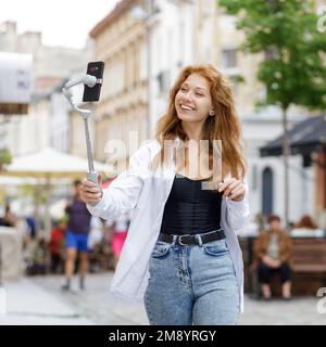 Junge rothaarige, schöne Frau, die läuft und ihr Handy benutzt Stockfoto