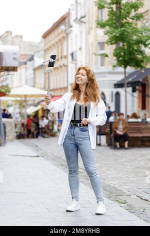 Junge rothaarige, schöne Frau, die läuft und ihr Handy benutzt Stockfoto