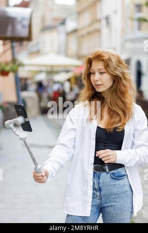 Junge rothaarige, schöne Frau, die läuft und ihr Handy benutzt Stockfoto