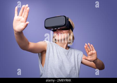 Lächelnde Frau, die ein VR-Headset trägt, das während des Virtual-Reality-Erlebnisses Luft berührt, isoliert auf violettem Hintergrund. Digitale Technologie Stockfoto