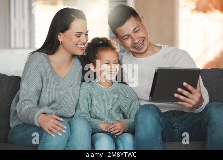 Die Welt, geheiratet entdeckt, liebt dich nicht so wie deine Familie. Eine junge Familie, die sich gerne mit einem digitalen Tablet zu Hause auf dem Sofa verbindet. Stockfoto