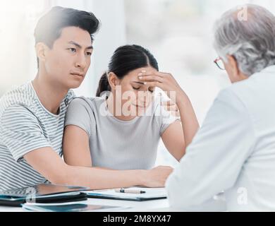 Leider war es kein Erfolg. Ein junges Paar, das bei seinem Arzt sitzt und während einer Sprechstunde in der Klinik verärgert aussieht. Stockfoto