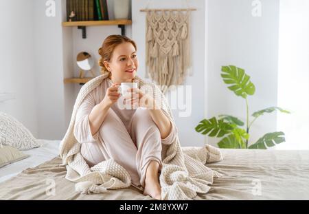 Porträt einer jungen Frau, die zu Hause eine Tasse Kaffee genießt. Hübsches Mädchen, das warme Getränke trinkt. Gute Zeit zu Hause. Stockfoto