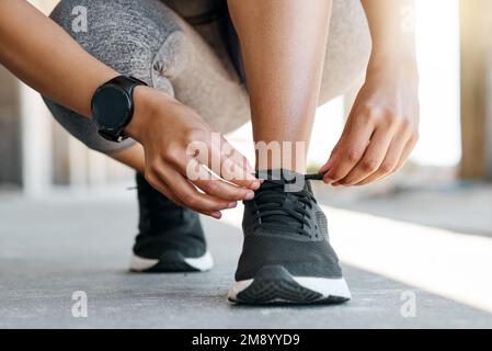 Ich will nicht stolpern. Eine unbekannte Frau, die sich während ihres Workouts im Freien unter den Füßen zusammenhockt, um ihre Schnürsenkel zu binden. Stockfoto