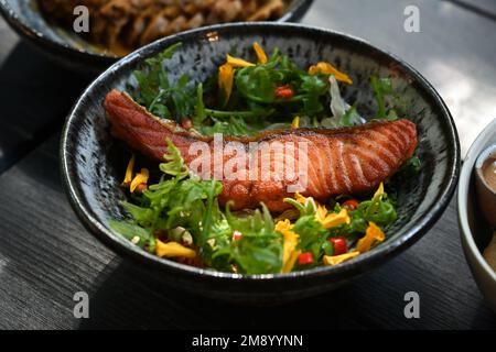 Blick aus der Nähe auf gebratenes Lachssteak mit essbaren Wildblumen und Gemüse auf einem Holztisch Stockfoto