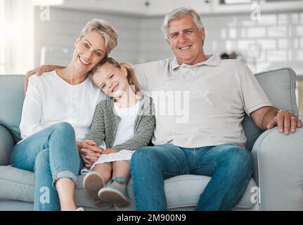 Liebe ist das größte Geschenk. Ein glückliches Seniorenpaar und ihre Enkelin entspannen sich zu Hause auf dem Sofa. Stockfoto