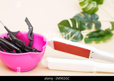 Professionelles Infrarot-Bügeleisen mit Friseurwerkzeugen zum Glätten und Erholen von Keratinhaaren auf beigem Hintergrund. Stockfoto