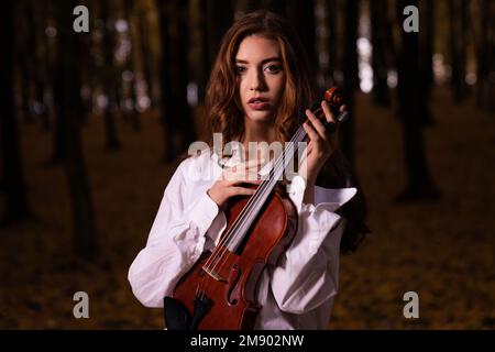 Eine weiße Frau, die im Wald Geige spielt Stockfoto