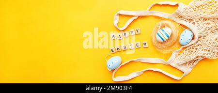 Inschrift Happy easter mit farbenfrohen, handgefertigten Eiern und Baumwollfäden auf orangefarbenem Hintergrund. Banner Stockfoto