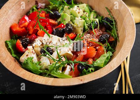 Frischer Salat mit Avocado, Tomaten, Mozzarella-Käse, Gemüsepaprika und schwarzen Oliven auf einer Holzschüssel. Stockfoto