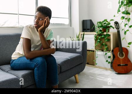 Junge schwarze Frau, die auf dem Sofa sitzt und sich Sorgen um persönliche Probleme macht Stockfoto