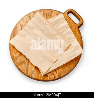 Backpapier auf Holzplatte isoliert. Rundes Brett mit zerknitterten Stücken braunem Pergament oder Backpapier auf weißem Hintergrund. Draufsicht. Design-Element Stockfoto