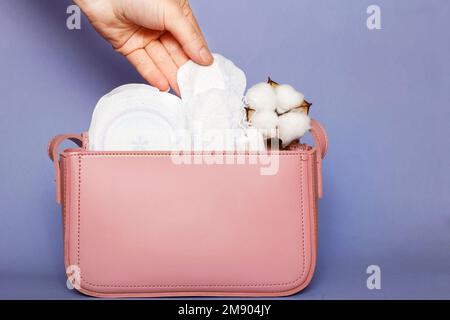 Die Damenhand entfernt das Slip-Futter aus der pinkfarbenen Kosmetiktasche mit Tampons und femininen Hygienepads. Stockfoto