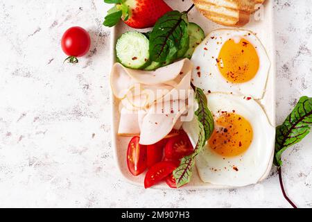 Spiegeleier mit Schinken, Tomaten, Gurken, Erdbeeren und Toast. Köstliches Englisches Frühstück. Brunch. Draufsicht, über Kopf Stockfoto