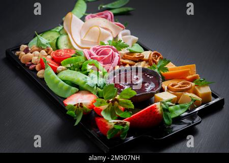 Vorspeisenplatte kaltgeschnittener Schinken, Salami, Cracker, Erdbeeren, Gemüse und Käseplatte an Bord vor dunklem Hintergrund. Vorspeisentisch mit Stockfoto