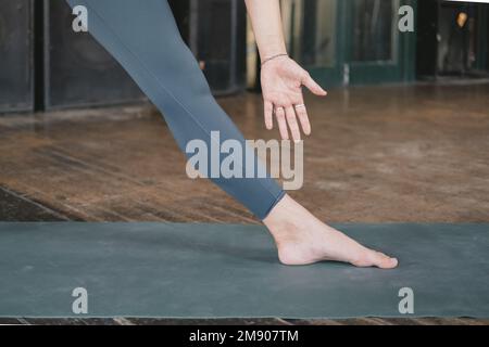 Nahaufnahme von Bein und Arm eines nicht wiedererkennbaren jungen Erwachsenen-Yoga und einer neuen Lehrerin, die eine Dreiecksstellung (Trikonasana) macht, Stretch- und Workout-Yoga Stockfoto