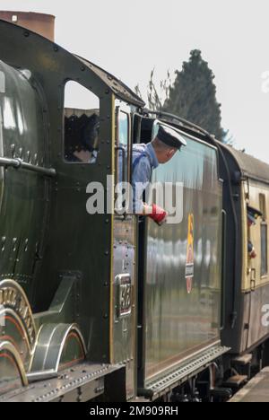 Der Zugführer lehnt sich aus seinem Taxi in der 1949 gebauten Dampfeisenbahn, modifizierte Halle Klasse 4-6-0*, Nr.7903 Foremarke Hall, kommt an der Toddington Rail Street an Stockfoto