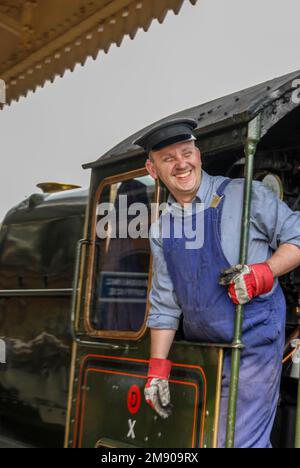 Der Zugführer lehnt sich aus seinem Taxi in der 1949 gebauten Dampfeisenbahn, modifizierte Halle Klasse 4-6-0*, Nr.7903 Foremarke Hall, kommt an der Toddington Rail Street an Stockfoto