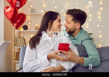 Glücklicher, gutaussehender junger Mann schenkt seinem attraktiven Liebhaber ein Geschenk zum Valentinstag, Geburtstag, Feiertag. Stockfoto