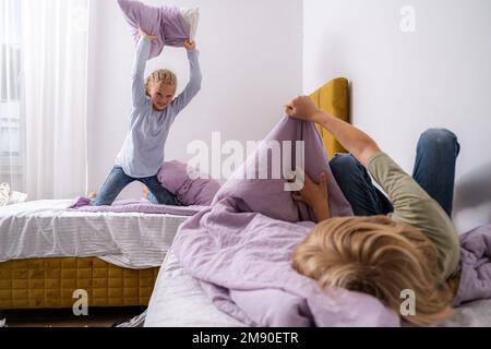 Geschwister, die Spaß haben, lachen, Junge und Mädchen spielen Kissenschlacht in einem dreckigen Kinderzimmer, Kinder spielen unter den vielen Spielzeugen zu Hause, viele Spielzeuge und Stockfoto