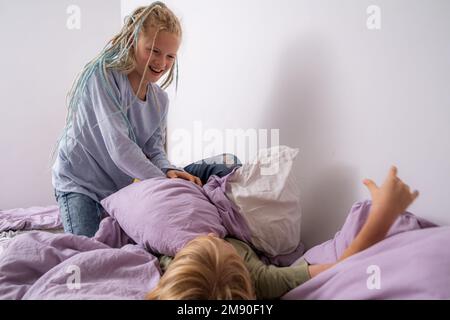 Geschwister, die Spaß haben, lachen, Junge und Mädchen spielen Kissenschlacht in einem dreckigen Kinderzimmer, Kinder spielen unter den vielen Spielzeugen zu Hause, viele Spielzeuge und Stockfoto