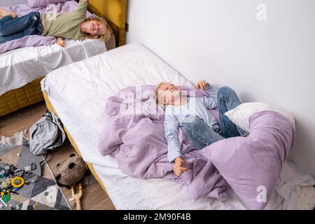 Geschwister, die Spaß haben, lachen, Junge und Mädchen spielen Kissenschlacht in einem dreckigen Kinderzimmer, Kinder spielen unter den vielen Spielzeugen zu Hause, viele Spielzeuge und Stockfoto