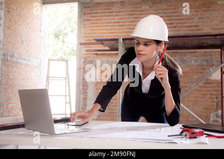 Junge, weiße Architektin, die auf einem Laptop sitzt und einen Entwurf für die Planung eines Gebäudes auf dem Schreibtisch zeichnet, Ingenieur denkt und skizziert blau Stockfoto