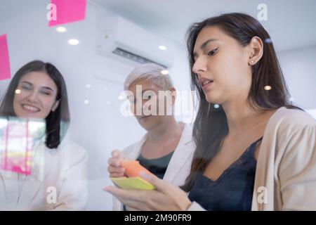 Gruppe von Team-Business-Mitarbeitern, die sich mit Haftnotizen über das Marketing im Büro, die Idee und das auf Glas stellen, Brainstorming und Meetings für die Planung durchführen Stockfoto