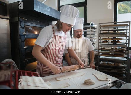 Ein Mann mit daunensyndrom, der mit seinem Kollegen Brot in der Bäckerei vorbereitete. Konzept der Integration von Menschen mit Behinderungen in die Gesellschaft. Stockfoto