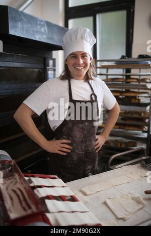 Junger Bäcker mit Koch-Kappe, der Gebäck in einer Bäckerei zubereitet. Stockfoto