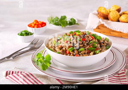 Pflanzenbasierte Version des US-amerikanischen Südgericht Hoppin John mit schwarzen Augenerbsen, braunem Reis, grünen Zwiebeln, rotem Paprika und Maisbrot-Muffins Stockfoto