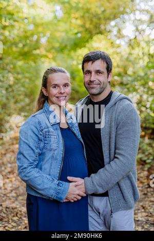 Porträt einer glücklichen schwangeren Frau und ihres Mannes, die im Wald stehen. Stockfoto
