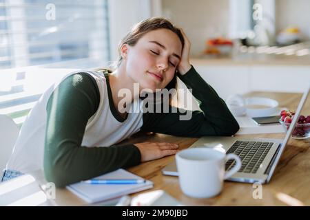 Junge Frau schläft während des Lernens an einem Tisch ein. Stockfoto