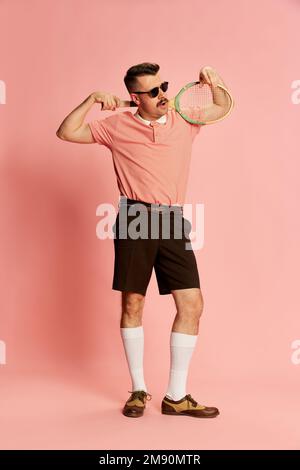 Elite-Sportverein. Porträts eines gutaussehenden charismatischen Mannes in stilvoller Kleidung mit Tennisschläger auf pinkfarbenem Studiohintergrund. Modebegriff Stockfoto