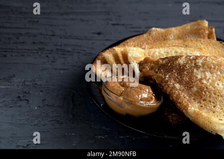 Fotografieren Sie etwas gebratene dreieckige Pfannkuchen mit Kondensmilch auf dunklem Hintergrund Stockfoto