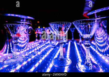 Gläser alkoholischer Cocktails bei der farbenfrohen Barkeeper-Show im Restaurant, beleuchtet mit Ultraviolett Stockfoto